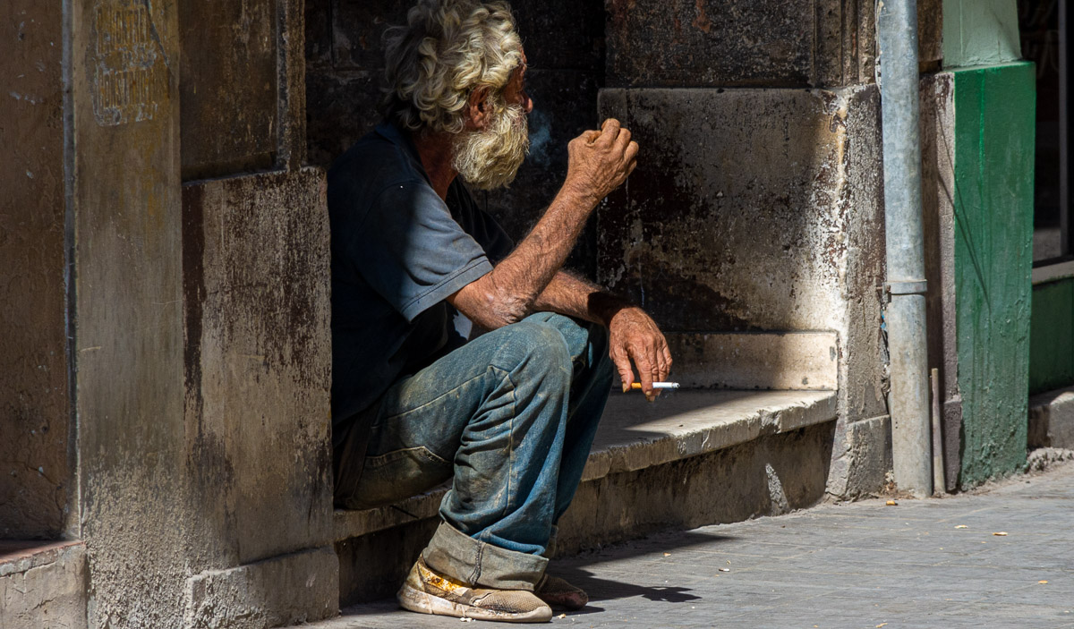 Anciano sentado en la acera.