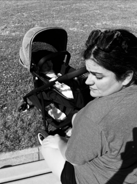 Mujer con expresión cansada sentada en el borde de una acera junto a un coche de bebé.