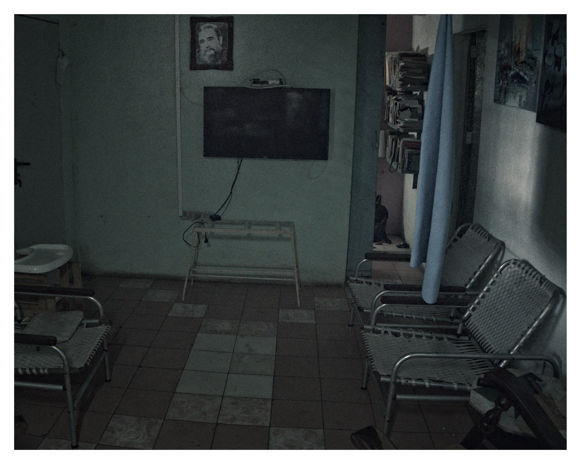 Sala vacía con sillas metálicas alineadas, un televisor apagado y un retrato de Fidel Castro en la pared.