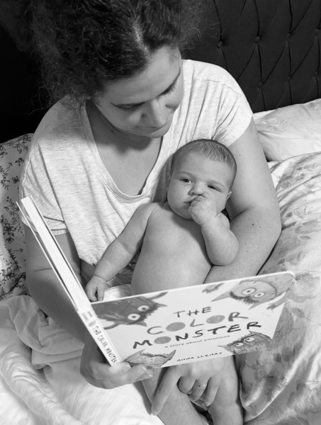 Mujer leyendo un libro sobre emociones a su bebé, quien la observa con curiosidad.