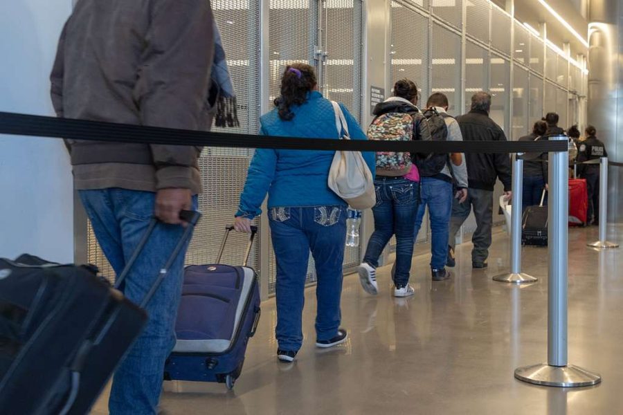 Personas en fila dentro de una instalación migratoria en Estados Unidos, con maletas y pertenencias personales.