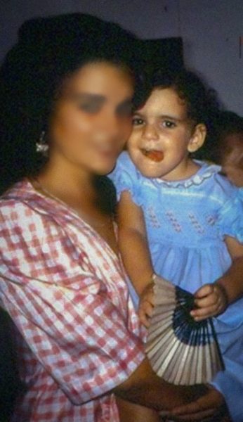 Madre joven con su hija pequeña en brazos, ambas visten vestidos y sonríen a la cámara.