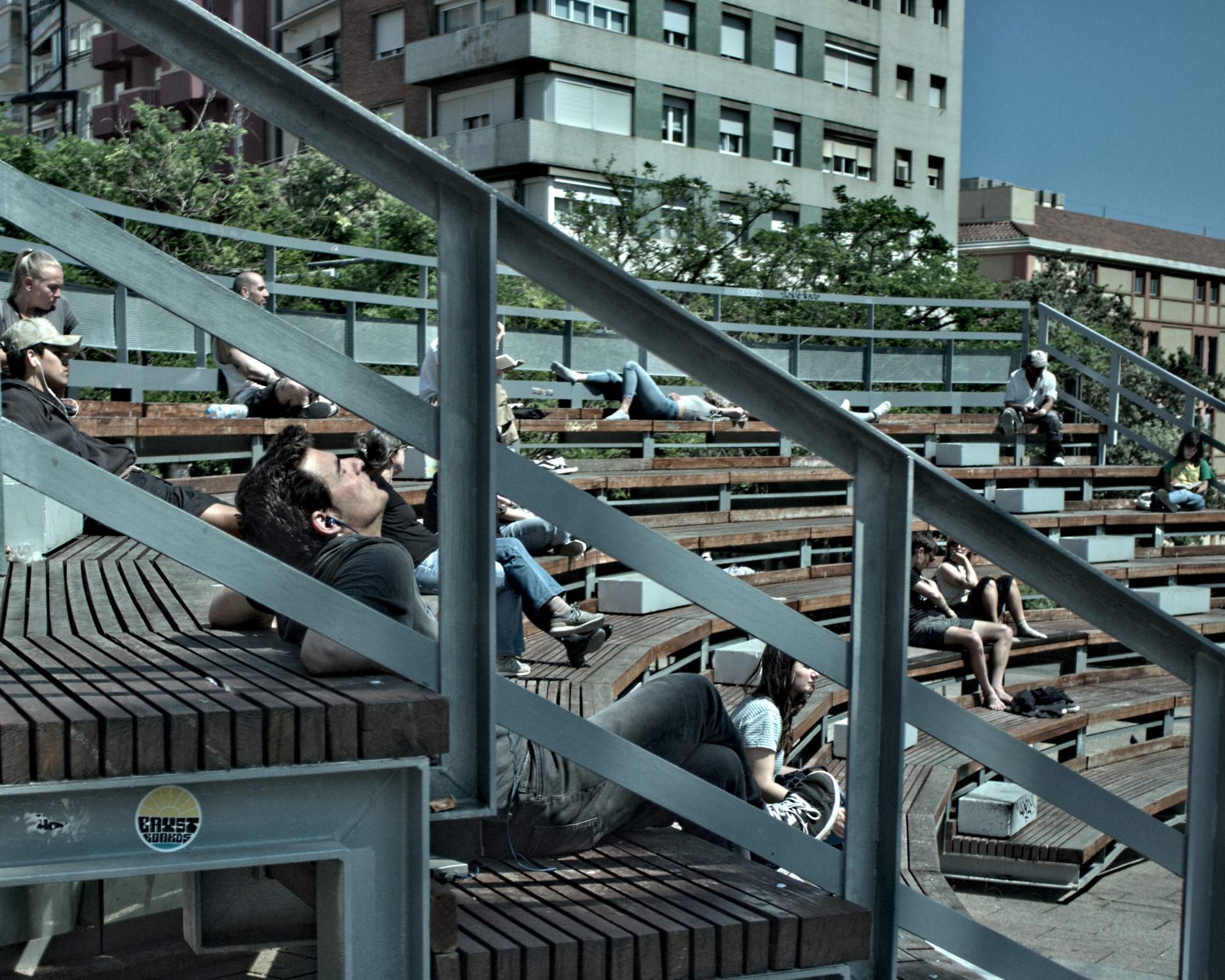 Personas sentadas en un anfiteatro urbano, muchas de ellas descansando bajo el sol.